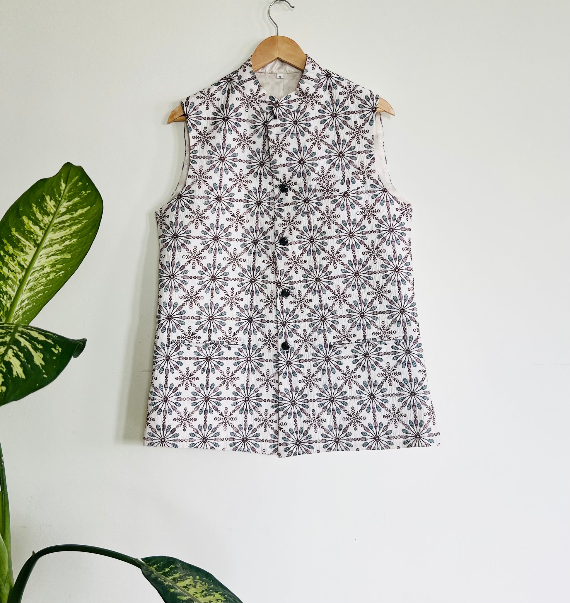 Black and white patterned sleeveless shirt on a hanger against a white background with a plant to the left.